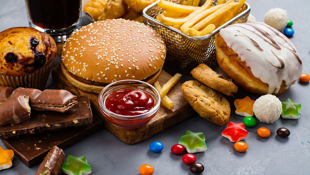 a photo of a pile of junk food, including a hamburger, fries, chocolate, gummy candy, a doughnut, cookies and more