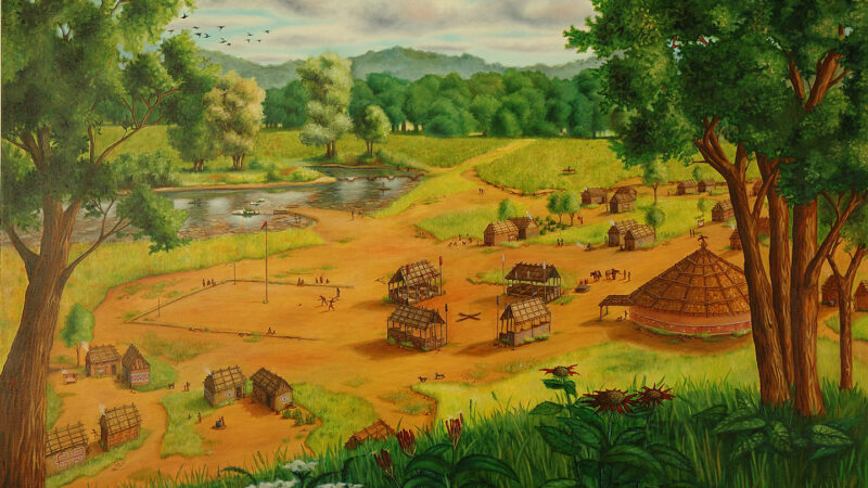 A painting of a Muscogee (Creek) village in the 1790s shows a circular council house next to four clan structures positioned around a square. The village is on the banks of a pond and surrounded by trees.