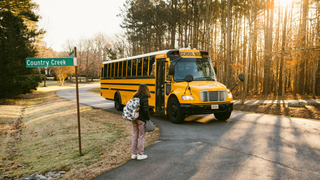A middle school student with shoulder length hair is waiting for a school bus that has just arrived in the early morning hours