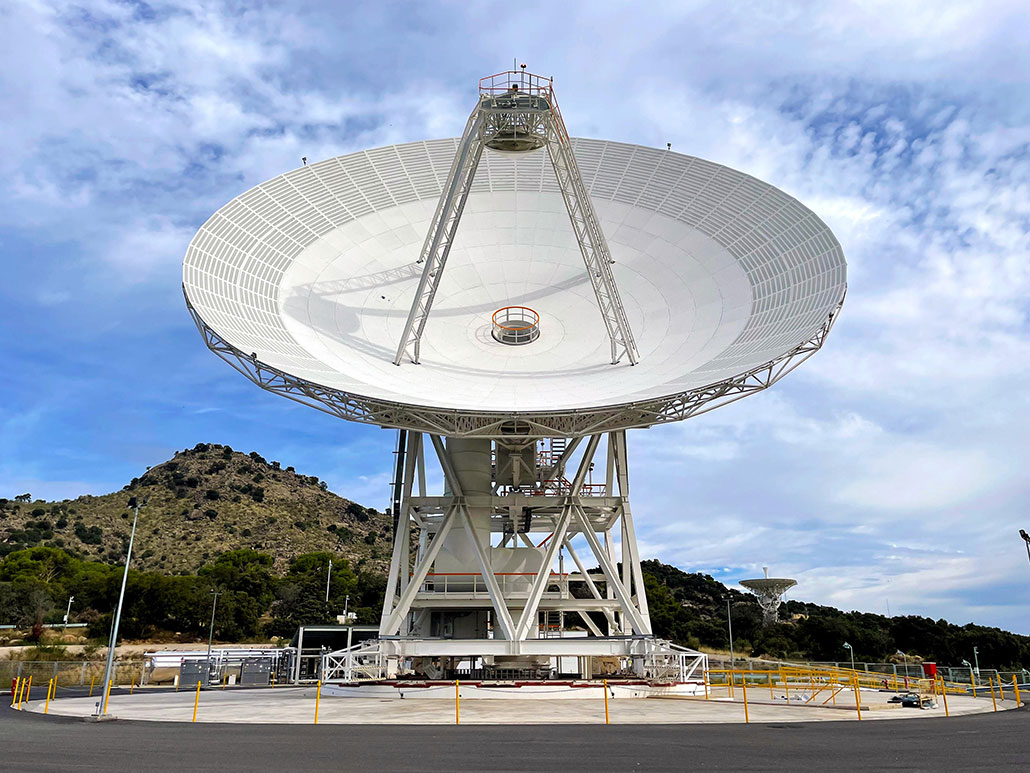 a huge radio telescope dish is pointed at a blue sky with white fluffy clouds