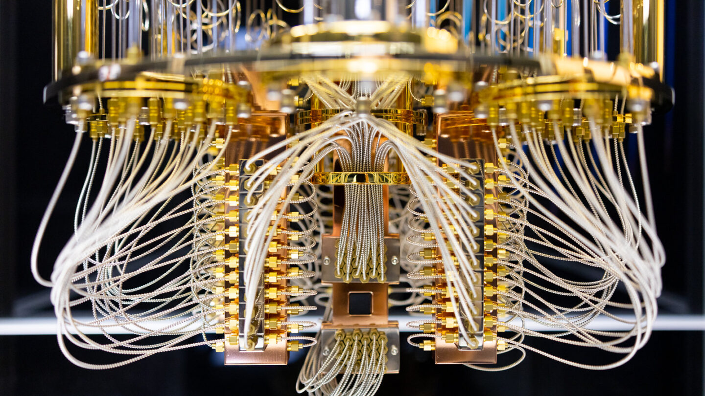 a circular structure with a shiny gold metal supports and silvery white wires runing throughout - it almost looks like a chandelier. At the very bottom there is a dark rectangle that all the wires seem to connect to, the quantum-processing chip.