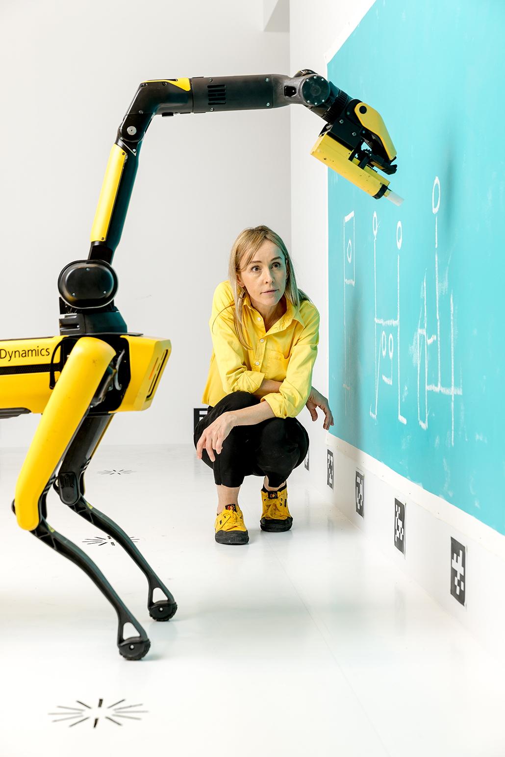 Agnieszka Pilat crouches next to a robot drawing with chalk as part of an art installation