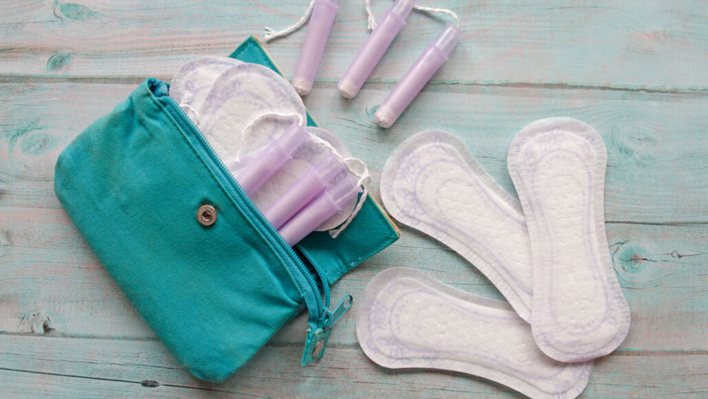 a few menstrual pads are spread out on a table alongside a teal bag that contains a few tampons and more pads