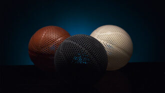 Three 3-D printed airless basketballs in black, brown and white against a dramatic studio background