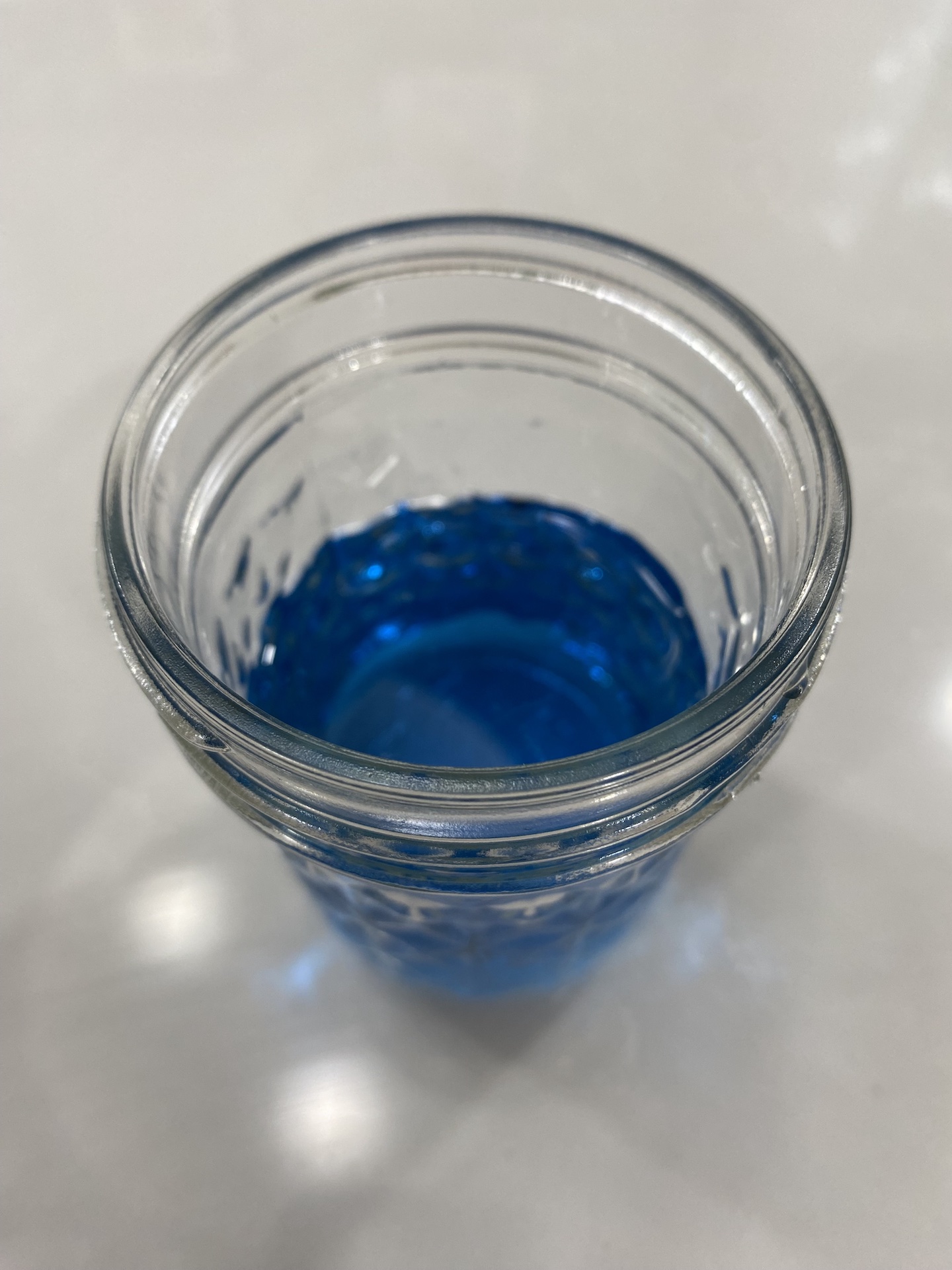 a glass jar is about half full of translucent blue liquid