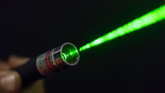 a hand holding a laser shines a green beam of light through the darkness