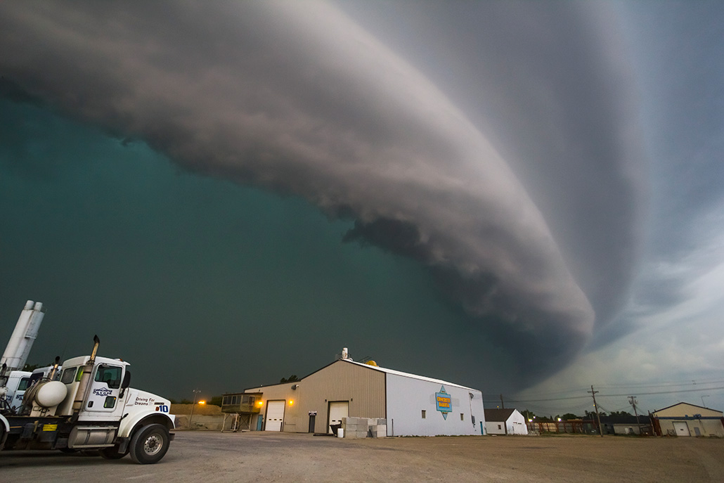 A curved row of clouds is shown in the sky above a building and truck.