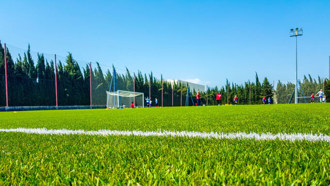 a close-up of artificial turf on a soccer field, soccer players can be seen in the distance