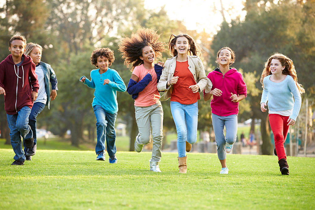 a bunch of boys and girls on a grassy field of mixed races running towards the viewer and smiling