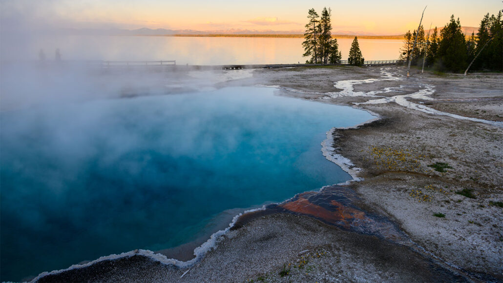 a clear pool of water with crystals at the edges is steaming as the sun sets