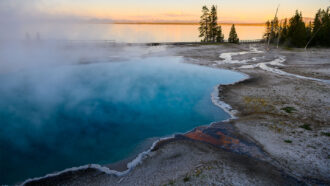 a clear pool of water with crystals at the edges is steaming as the sun sets