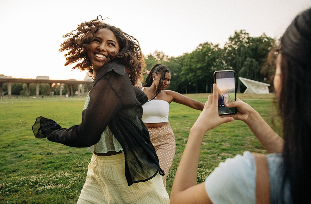 two girls dancing in a field as their friend films them on a phone