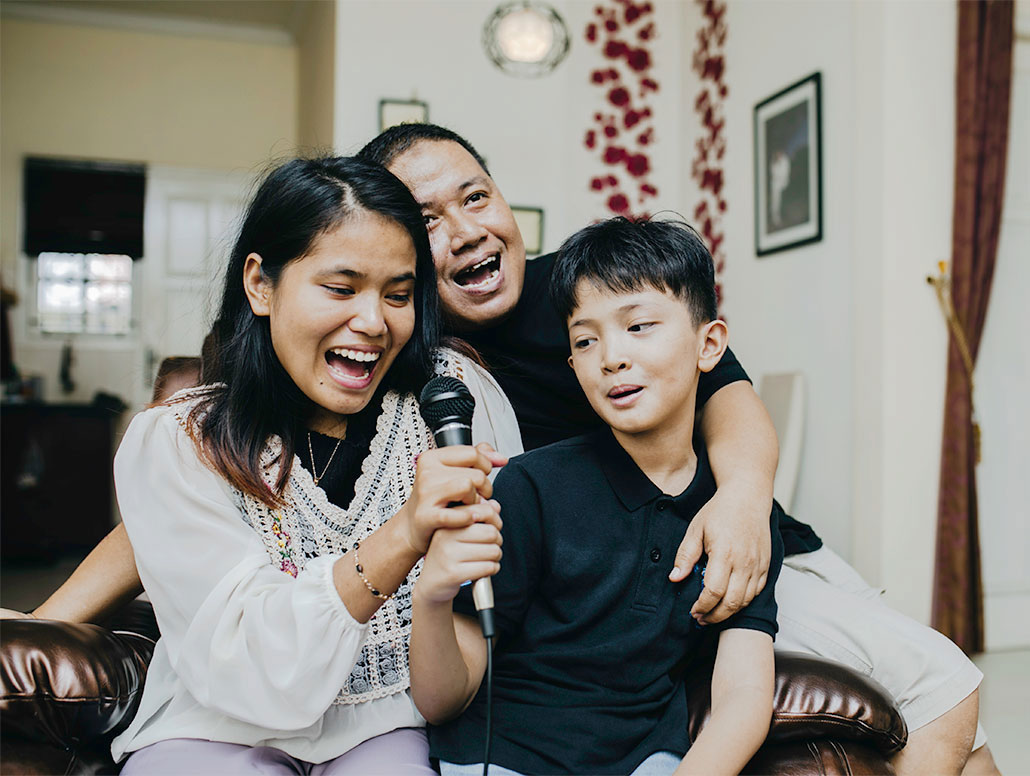 a family shares the microphone as they sing a karaoke song into a microphone at home