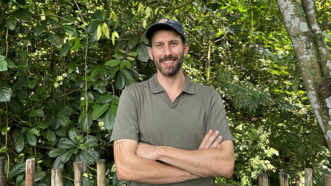 Elias Garcia Pelegrin stands in front of a tropical forest. He has light brown hair and a beard. He is wearing a green polo shirt and matching baseball cap.