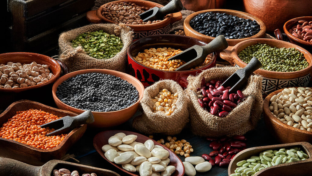 an array of dried beans and legumes arrangesd on a rustic wooden table in bowls and sacks