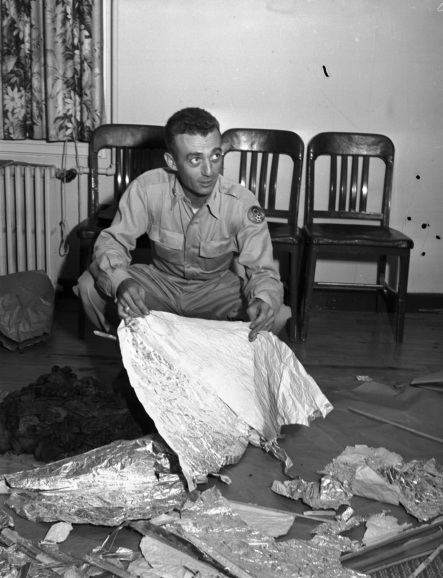 a black and white photo of a man in uniform inspecting shiny debris on the floor