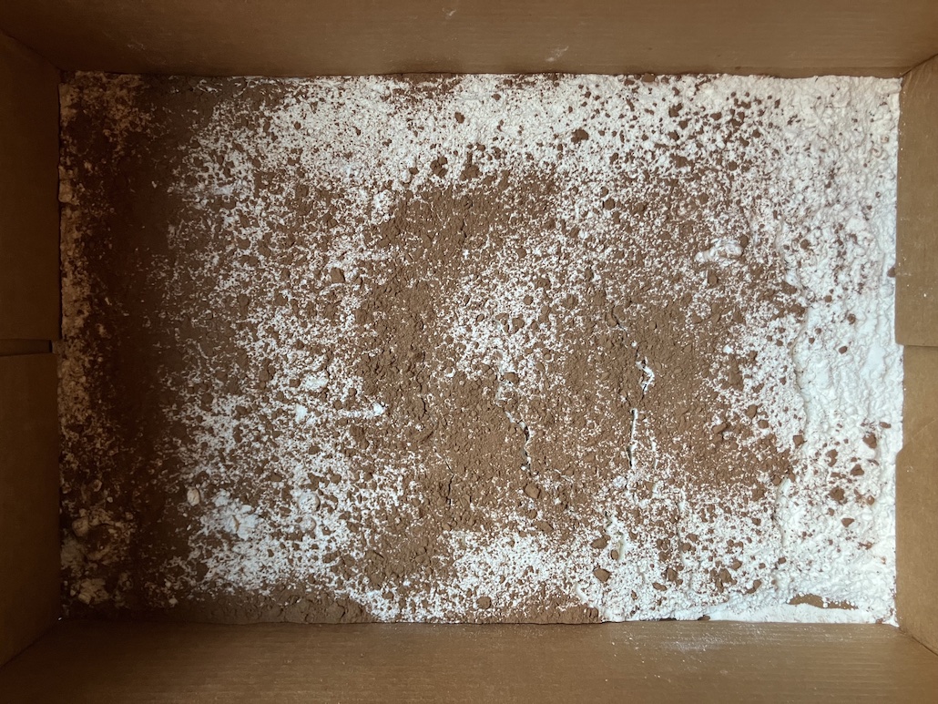 a box containing a layer of white flour with a sprinkling of brown cocoa powder over the top