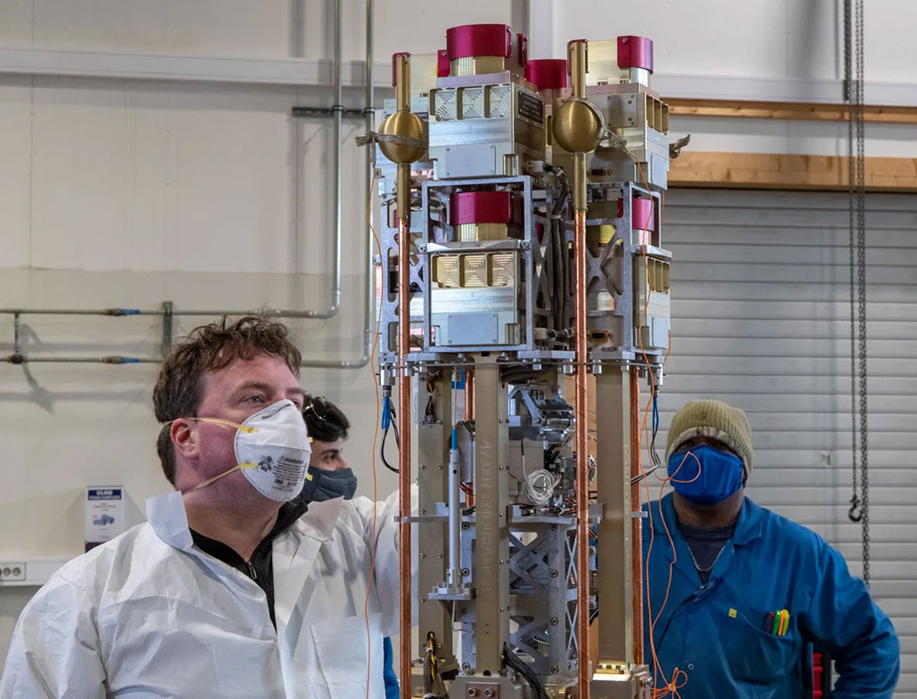 a photo of a white male scientists in a white lab coat and N95 face mask checking a tall electronic apparatus 