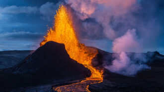 a picture of lava shooting out of a volcano and flowing away in a stream