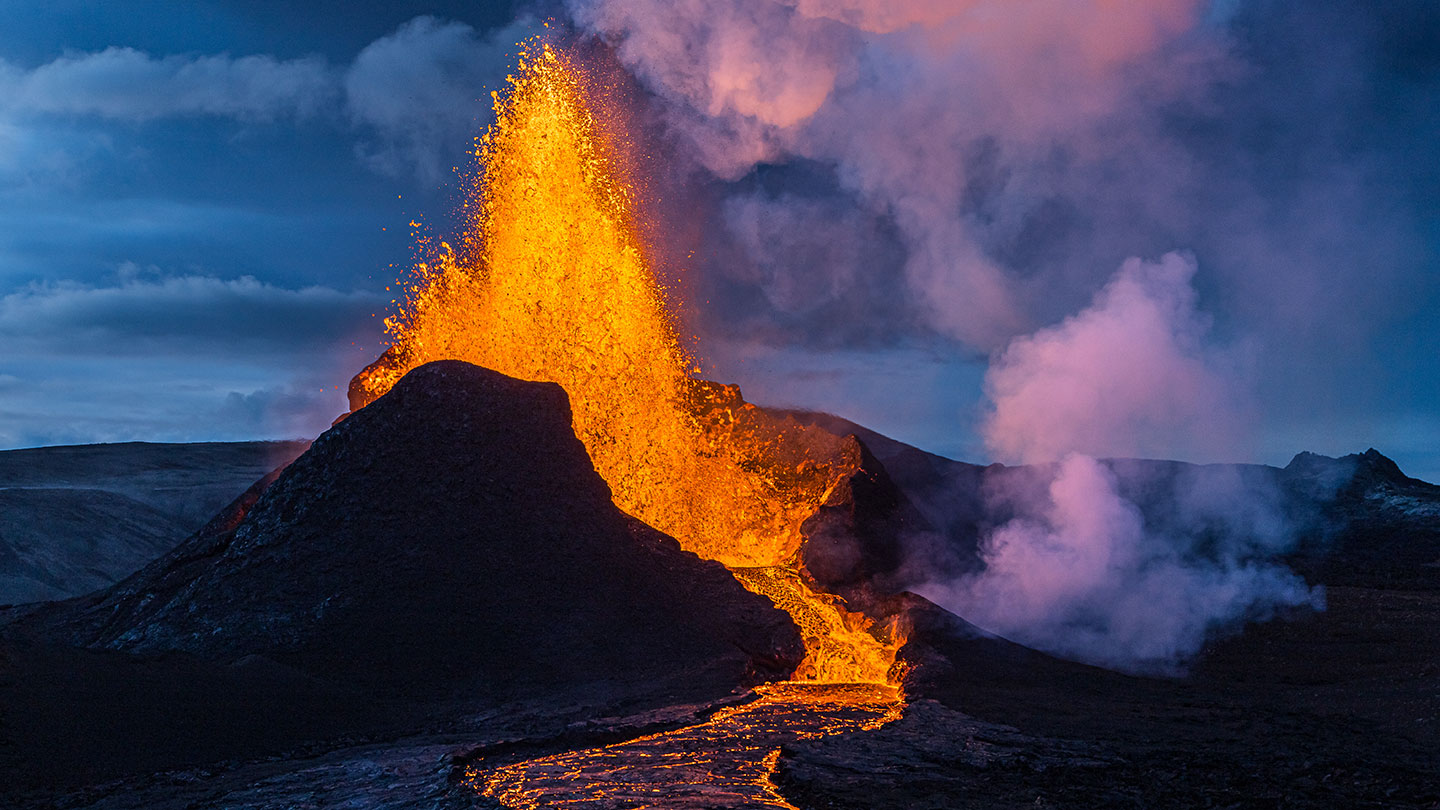 a picture of lava shooting out of a volcano and flowing away in a stream