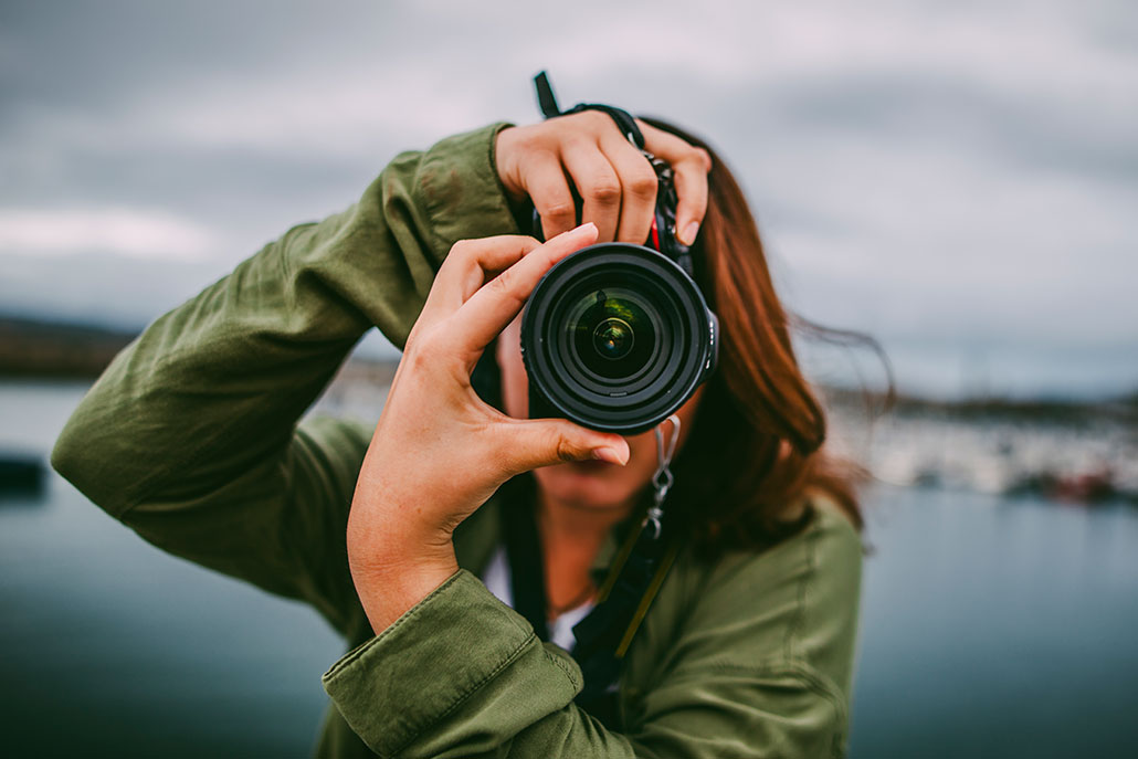 a woman holding a dslr camera with the lens pointed at the viewer