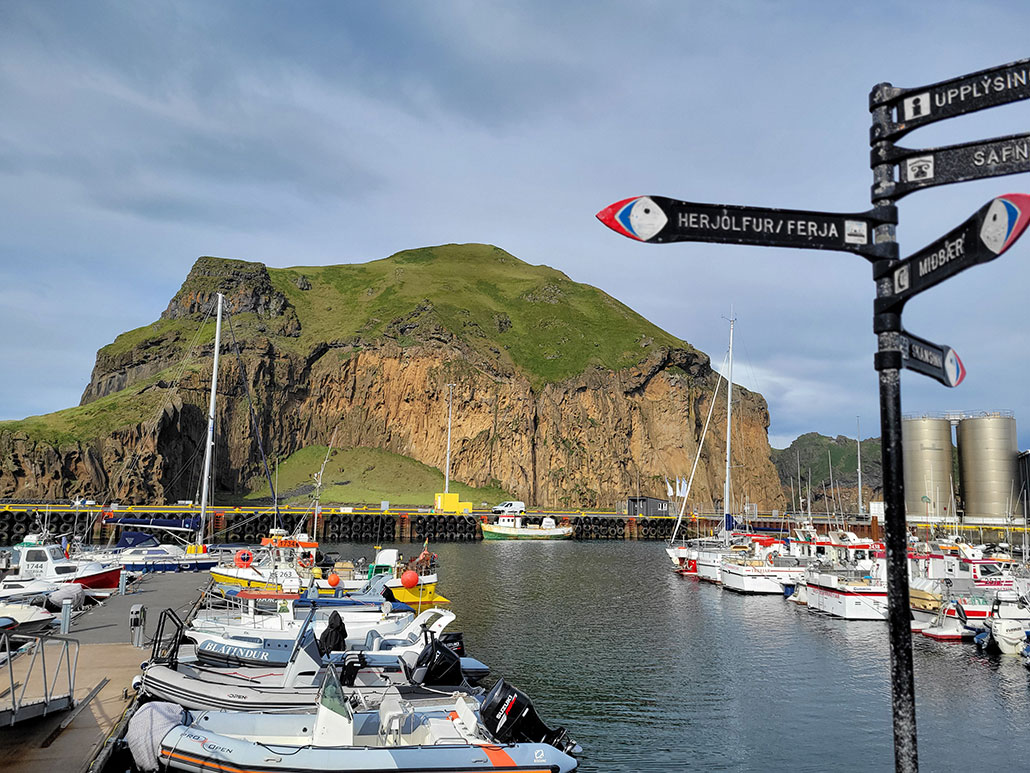 a photo of a harbor in Heimaey, Iceland. A signpost to the right in the image has puffin shaped arrows